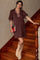woman wearing a brown maternity dress with puff sleeves and plaid details, posed on a staircase with a book in hand