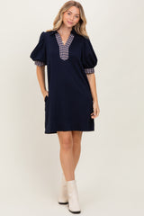 woman wearing a navy short sleeve dress with a checkered collar and puff sleeves, standing and smiling