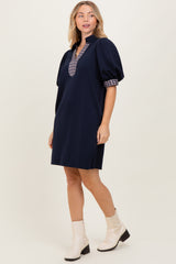 woman wearing a navy blue short sleeve collared dress with plaid detail and puff sleeves, paired with cream ankle boots