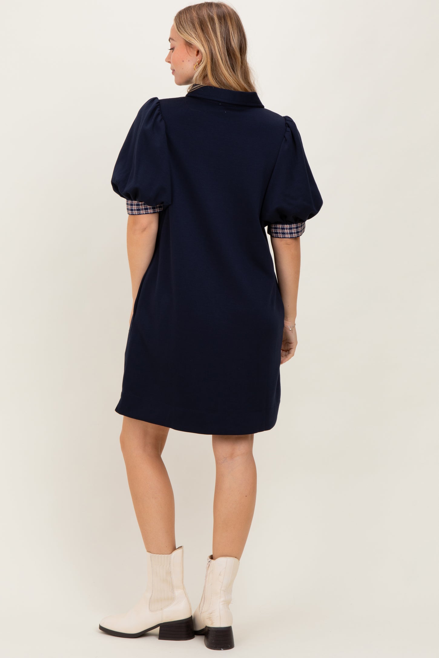 woman wearing a navy blue dress with puff sleeves and plaid details, viewed from the back, paired with white ankle boots