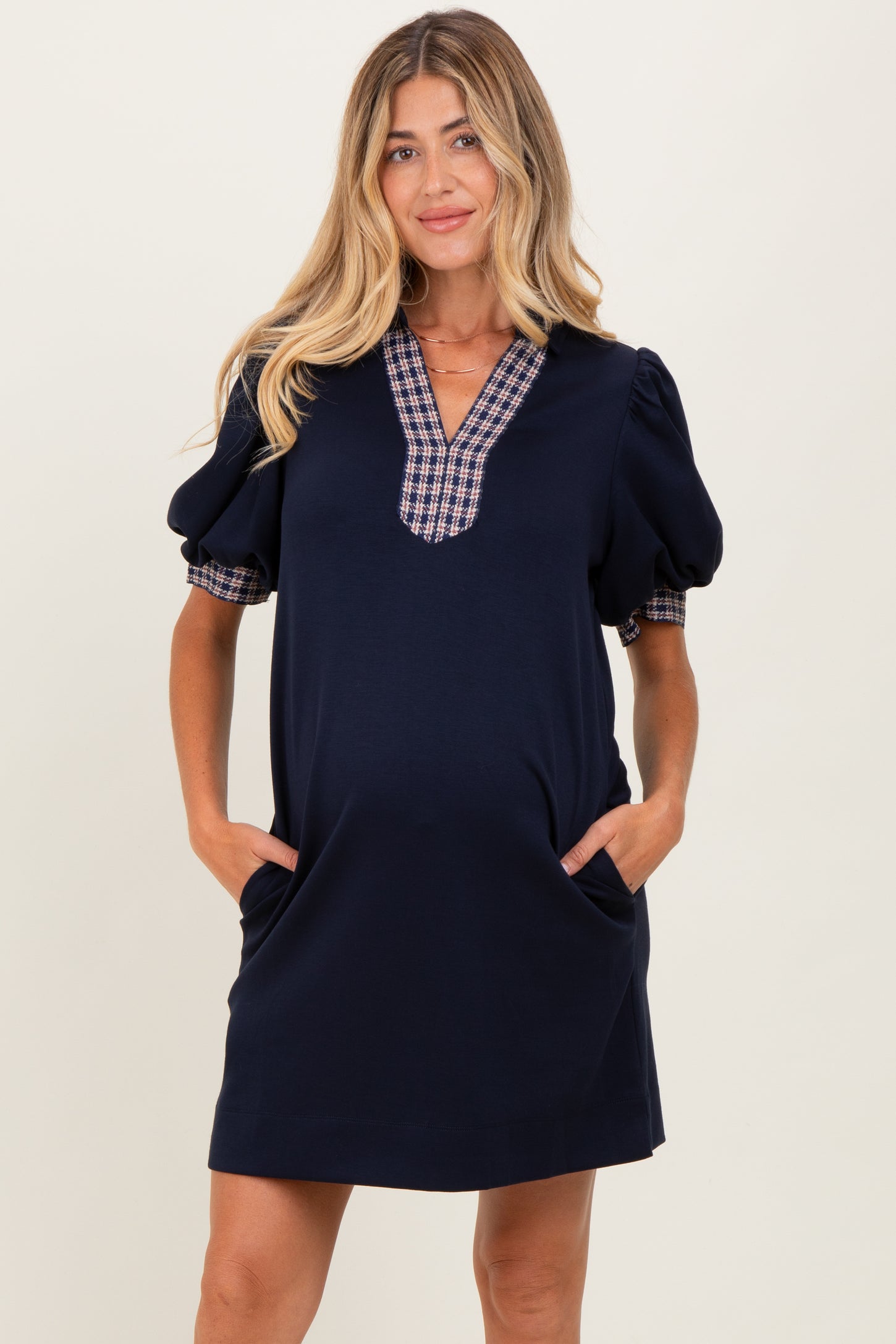 woman wearing a navy blue maternity dress with puff sleeves and plaid detailing, featuring pockets and a visible baby bump