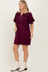 woman wearing a burgundy short sleeve zip-up dress with oversized sleeves and a gold zipper detail