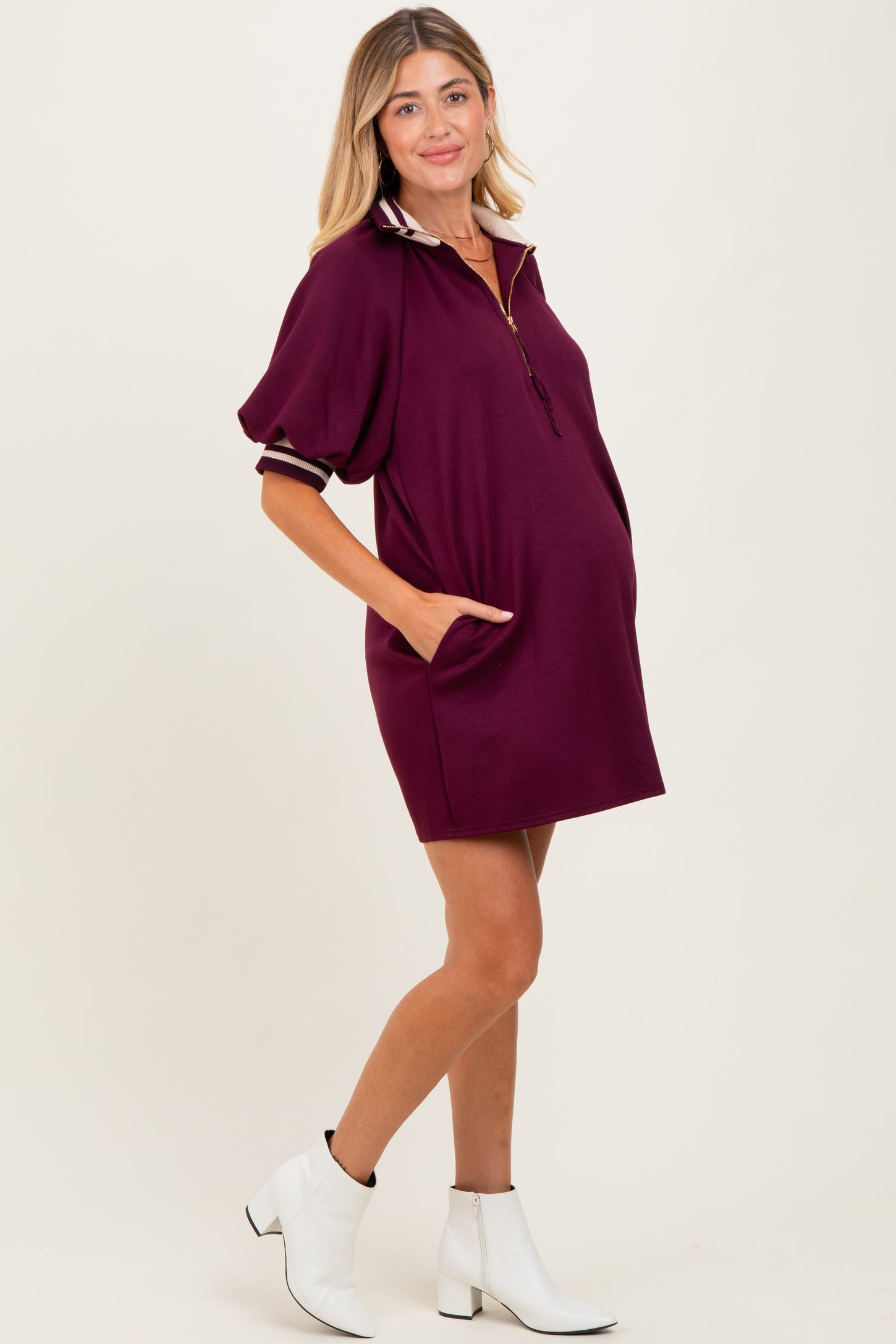 woman wearing a burgundy maternity polo dress with pockets and a half-zip collar, showing her baby bump