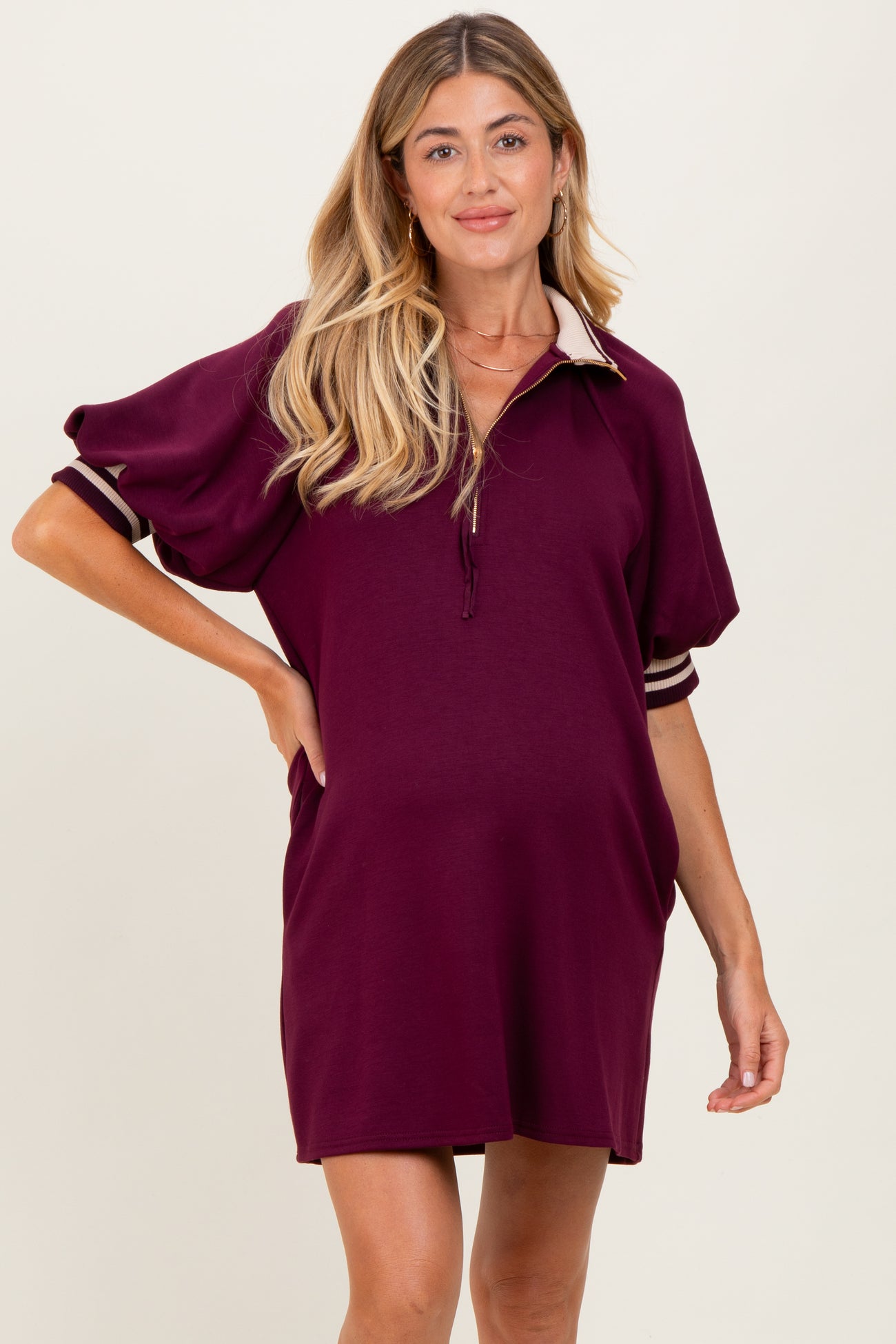 woman wearing a burgundy maternity polo dress with short sleeves and side pockets, showing her baby bump