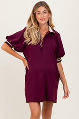 woman wearing a burgundy maternity polo dress with short sleeves and side pockets, showing her baby bump