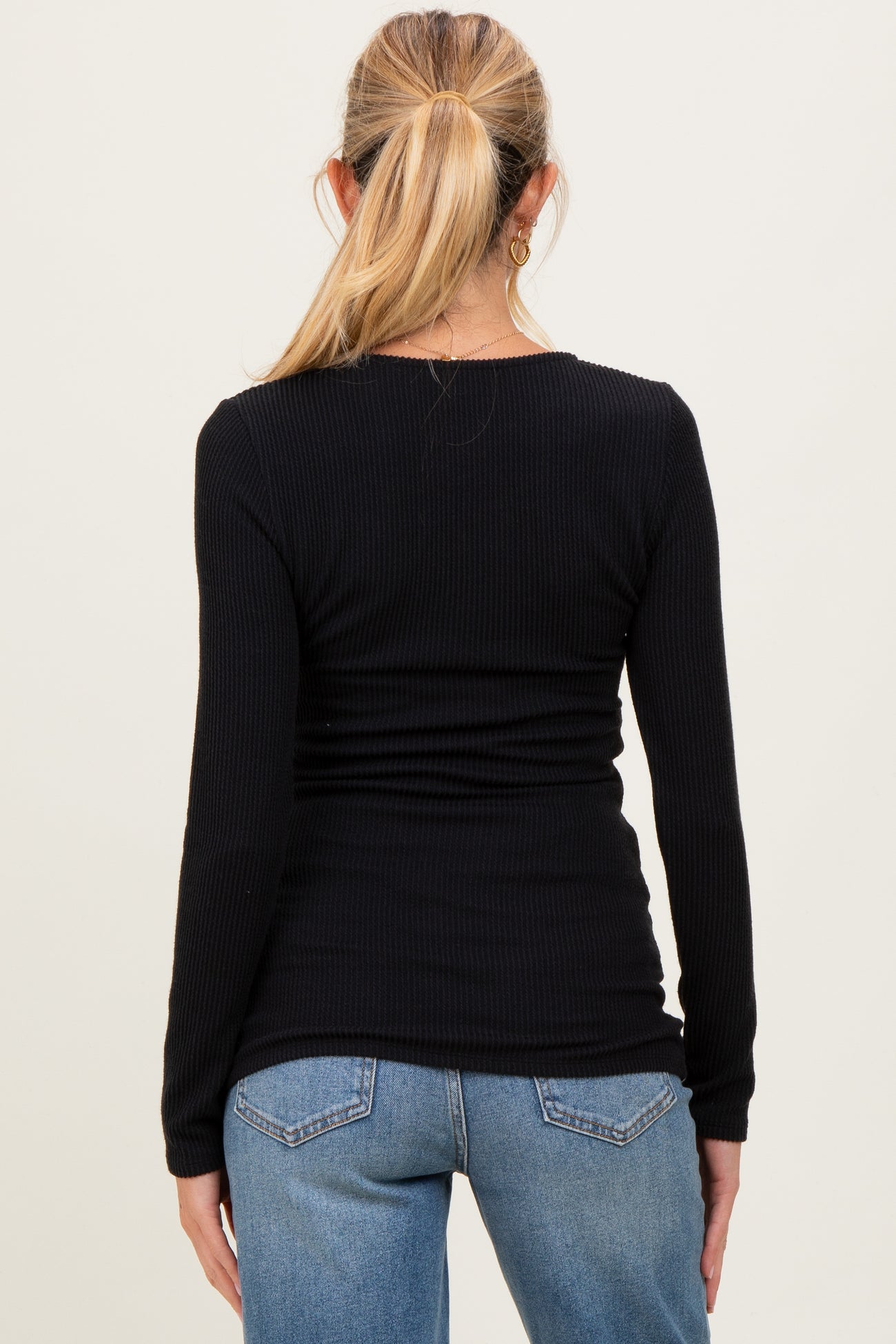 woman wearing a black long sleeve ribbed maternity top, seen from the back with denim jeans