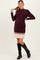 woman wearing a burgundy ribbed maternity dress with pleated bottom and long sleeves, showing her baby bump