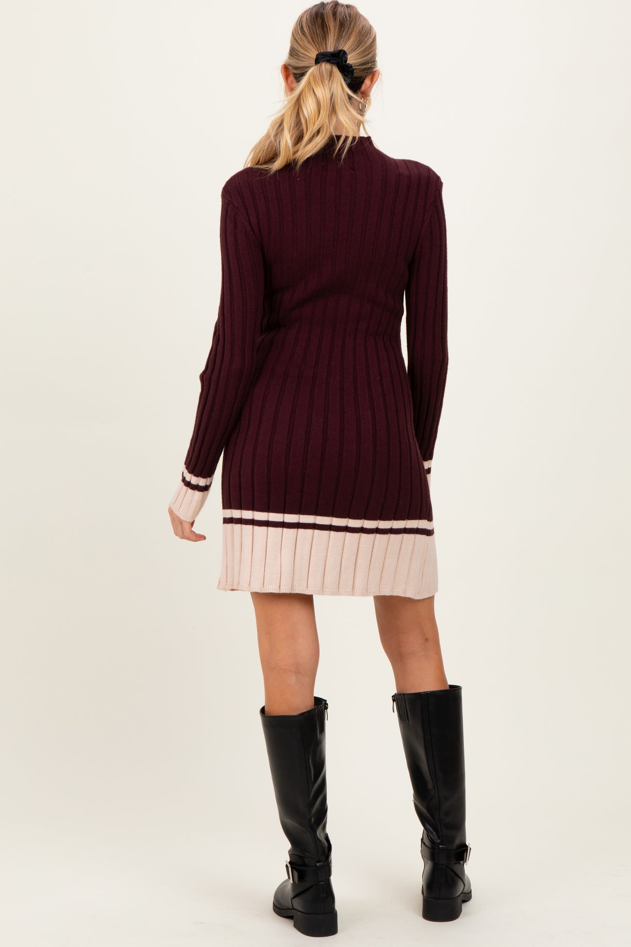 woman wearing a maroon ribbed maternity dress with a pink striped hem and long sleeves, showing off the baby bump