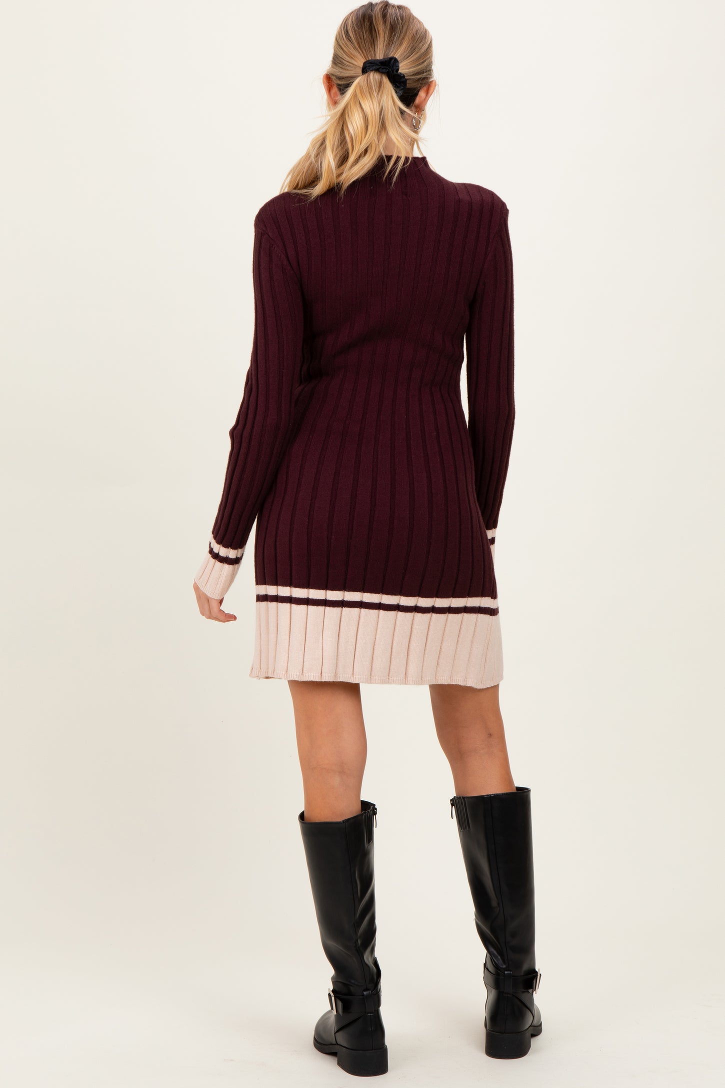 woman wearing a maroon ribbed maternity dress with a pink striped hem and long sleeves, showing off the baby bump