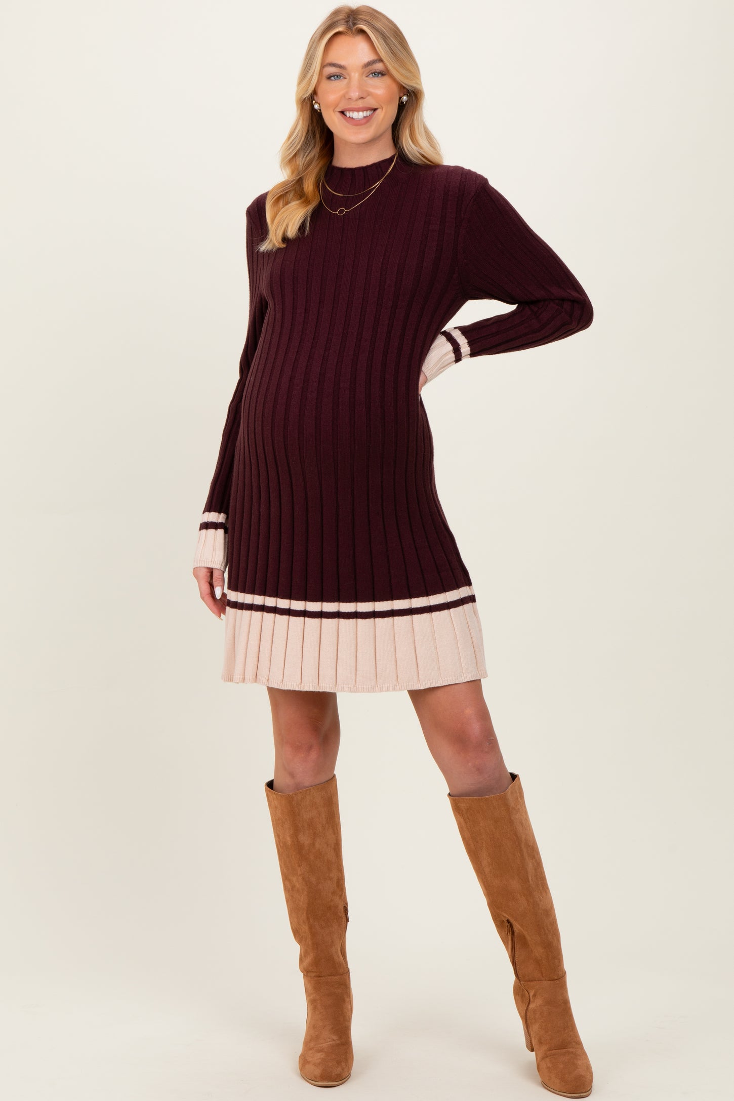 woman wearing a burgundy and cream striped maternity sweater dress with a ribbed texture and knee-high boots, showing her baby bump
