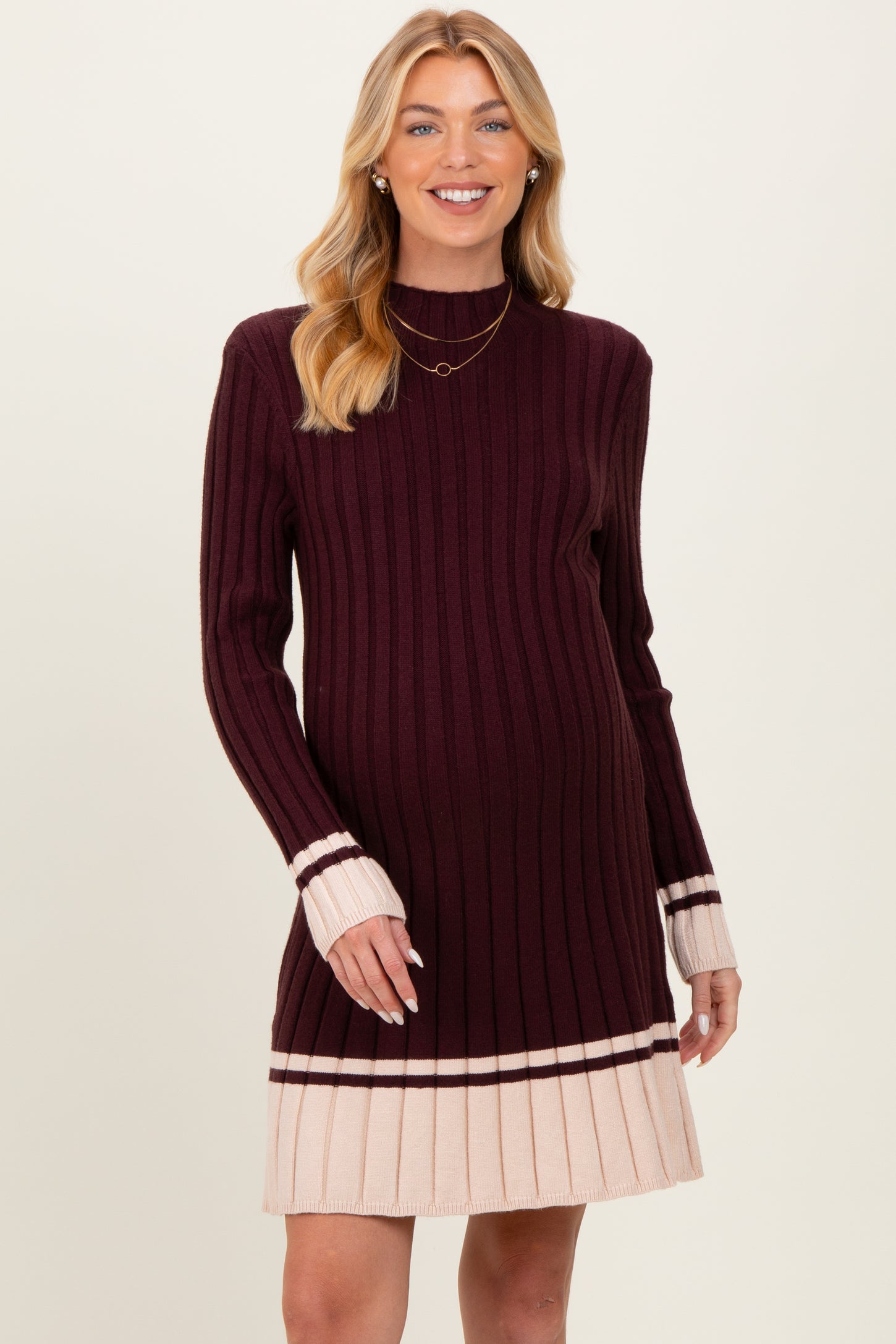 woman wearing a maroon and cream maternity sweater dress with a ribbed texture and long sleeves, showing her baby bump
