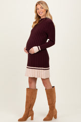 woman wearing a maroon ribbed maternity dress with a beige striped hem and holding her baby bump