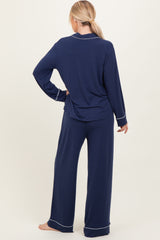 woman wearing a navy blue long sleeve pajama top and matching wide-leg pants with white piping details, viewed from the back