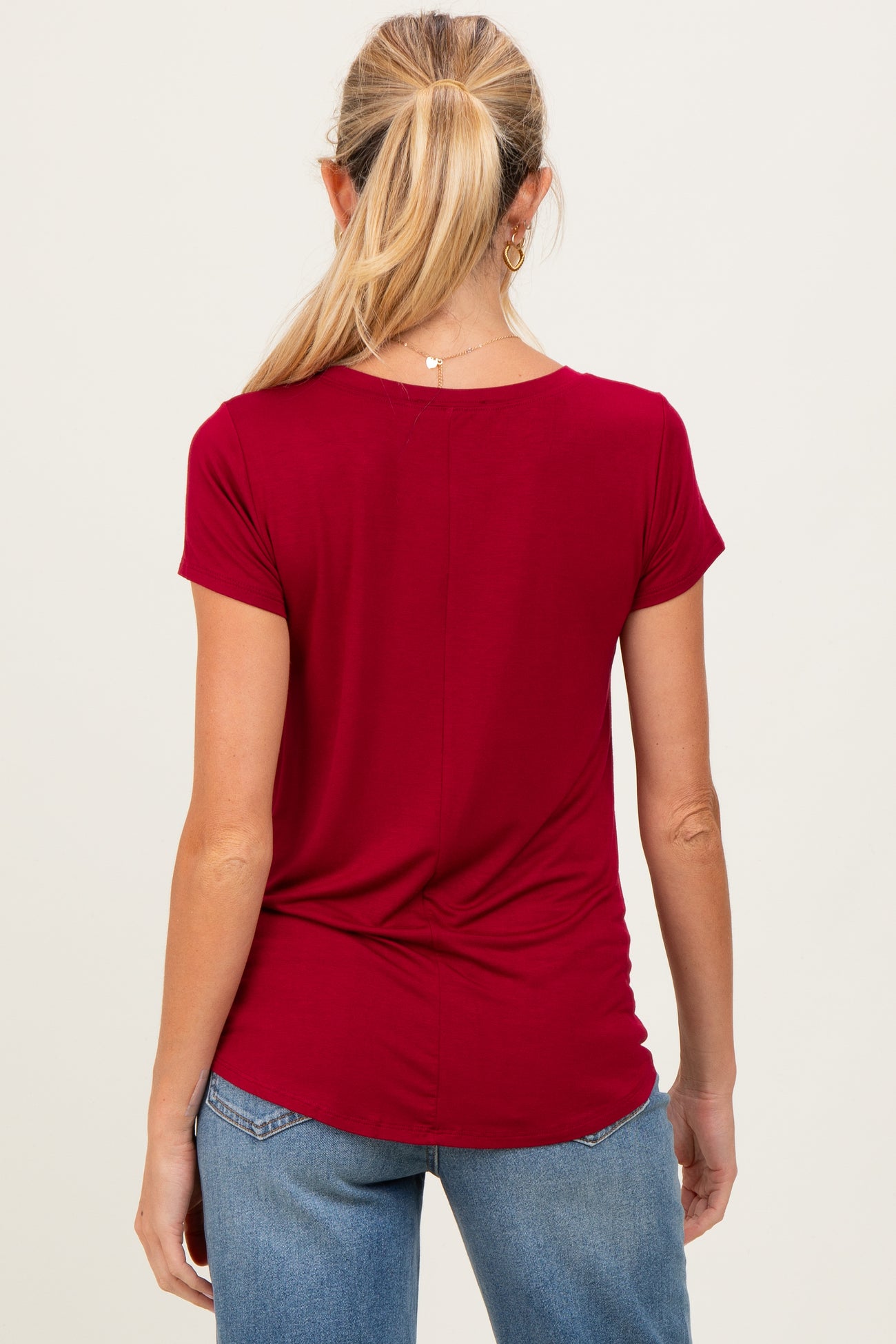 woman wearing a red short sleeve maternity top, shown from the back, with a gathered detail at the waist