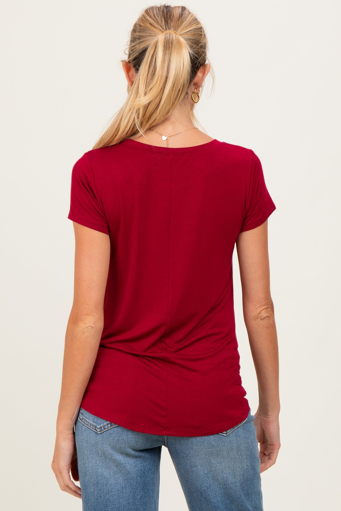 woman wearing a red short sleeve maternity top, shown from the back, with a gathered detail at the waist