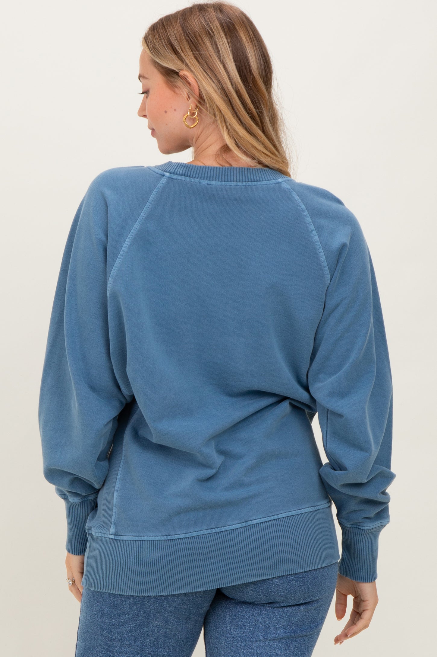 woman wearing a blue oversized sweatshirt with balloon sleeves and ribbed hem, viewed from the back