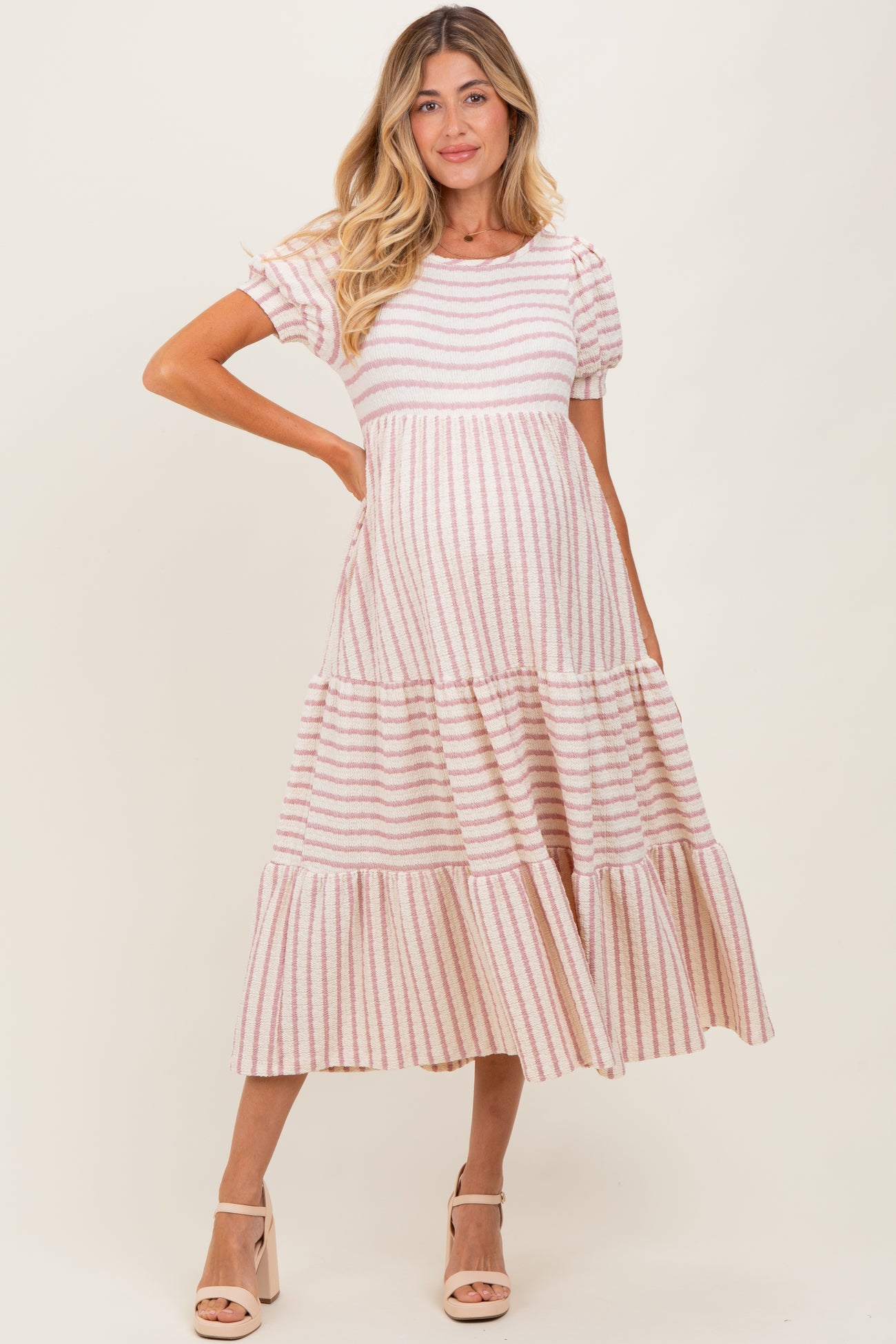 woman wearing a pink and white striped maternity dress with short puff sleeves and a tiered skirt, showing her baby bump