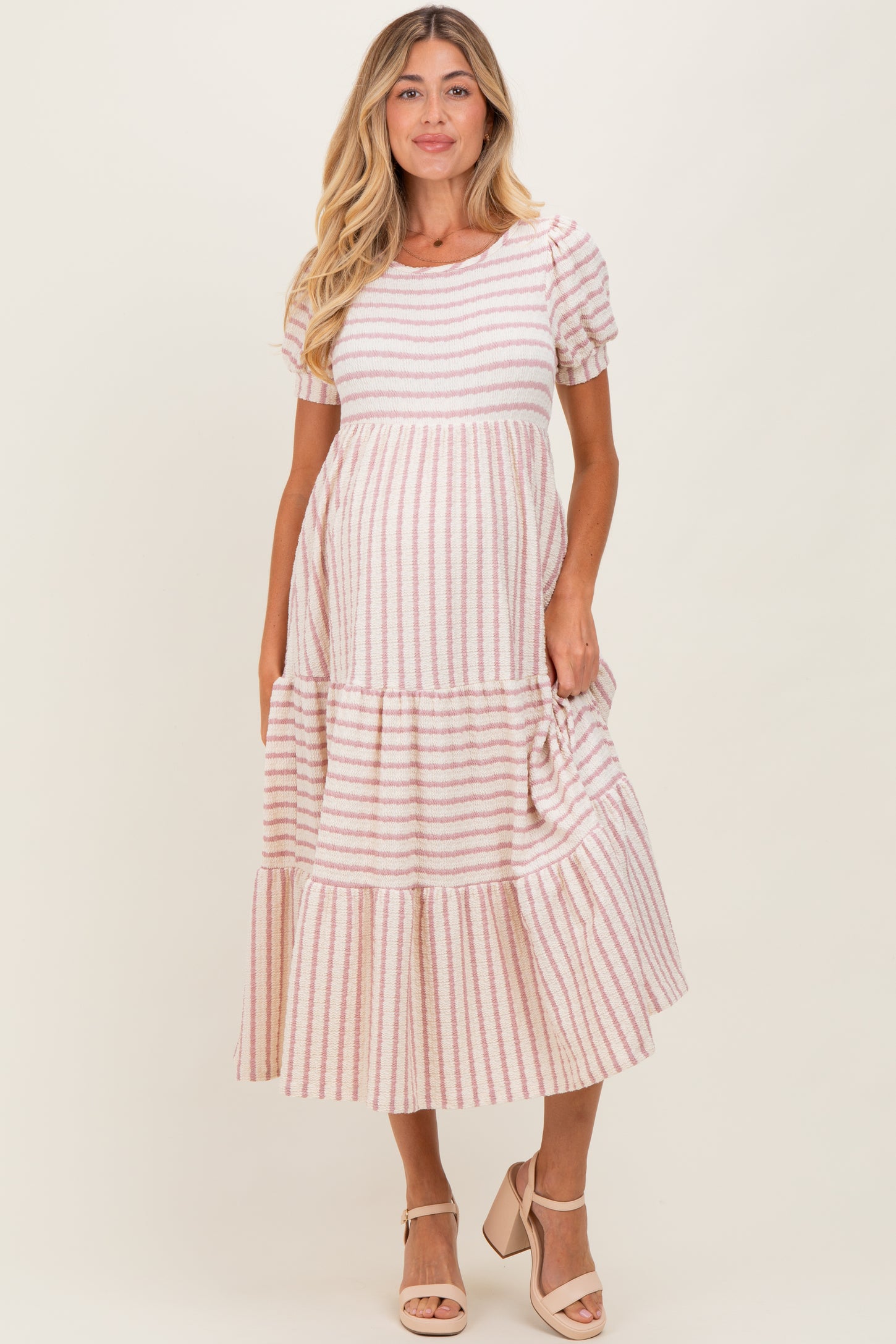 woman wearing a pink and white striped maternity dress with short sleeves and a tiered skirt, holding her baby bump