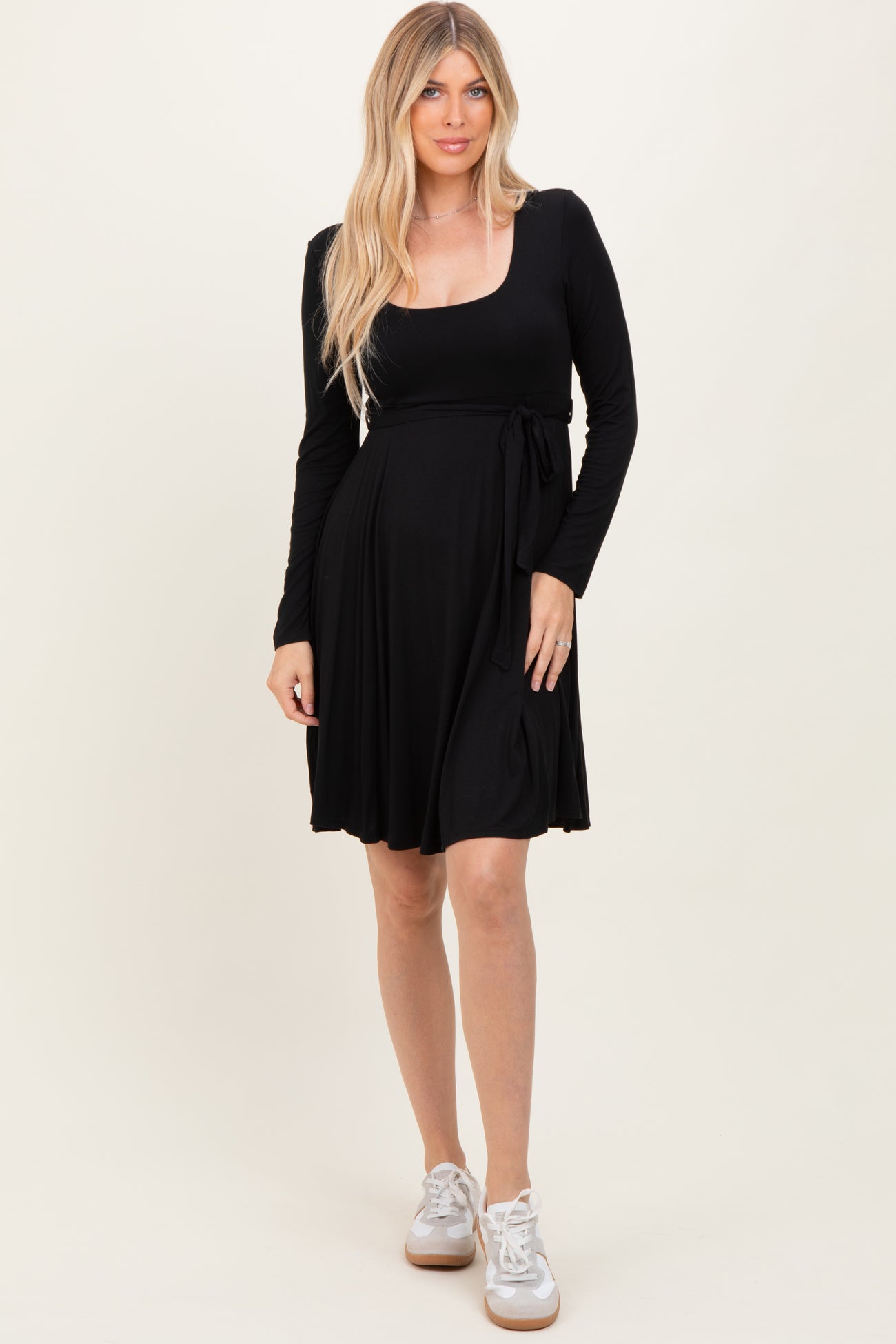 woman wearing a black long sleeve wrap dress with a tie detail at the waist and white sneakers