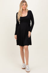 woman wearing a black long sleeve wrap dress with a tie detail at the waist and white sneakers