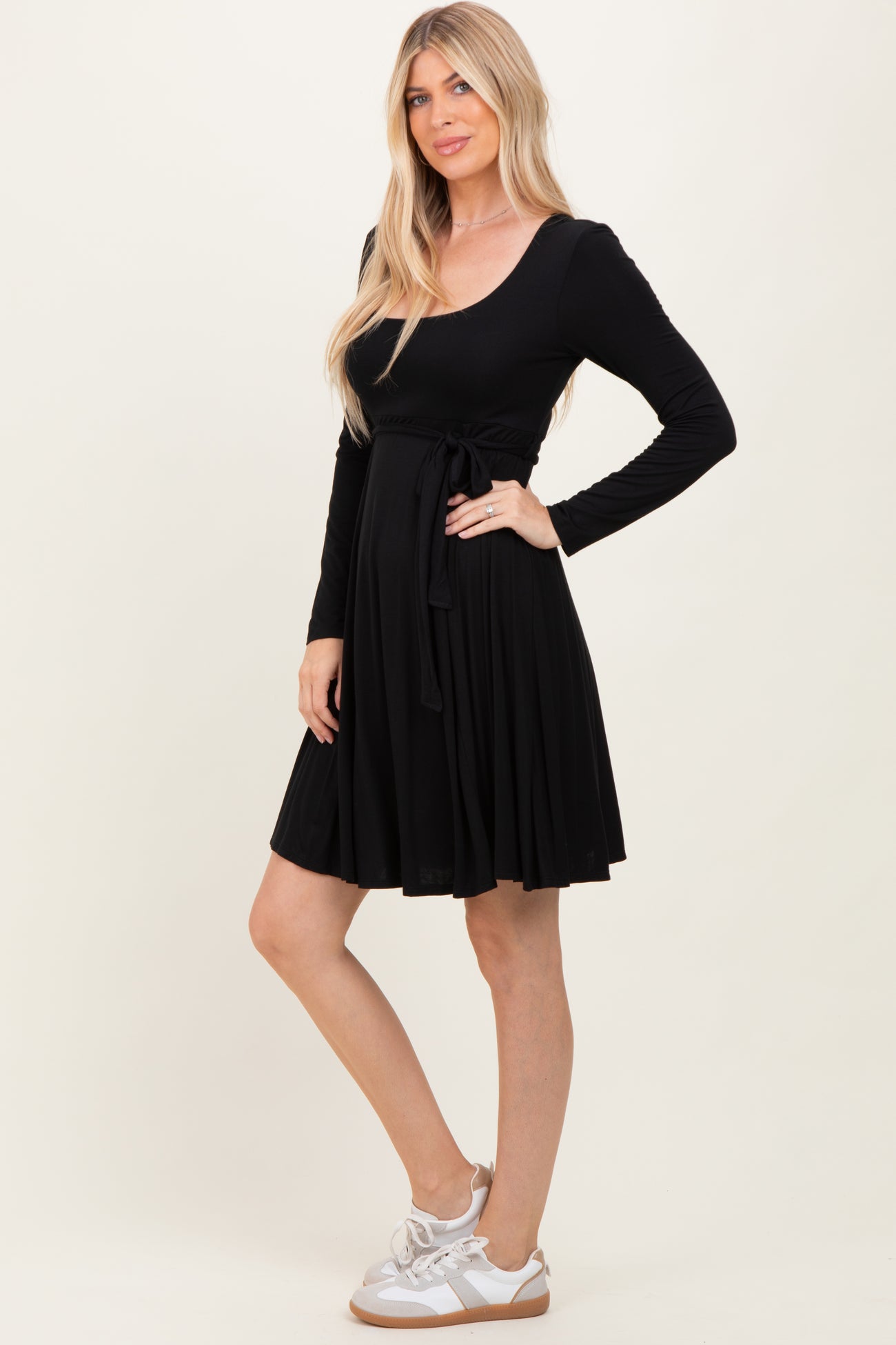 woman wearing a black long sleeve dress with a fitted waist and a flowy skirt, paired with white sneakers