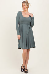 woman wearing a long sleeve sage green dress with a scoop neckline and a tie belt at the waist