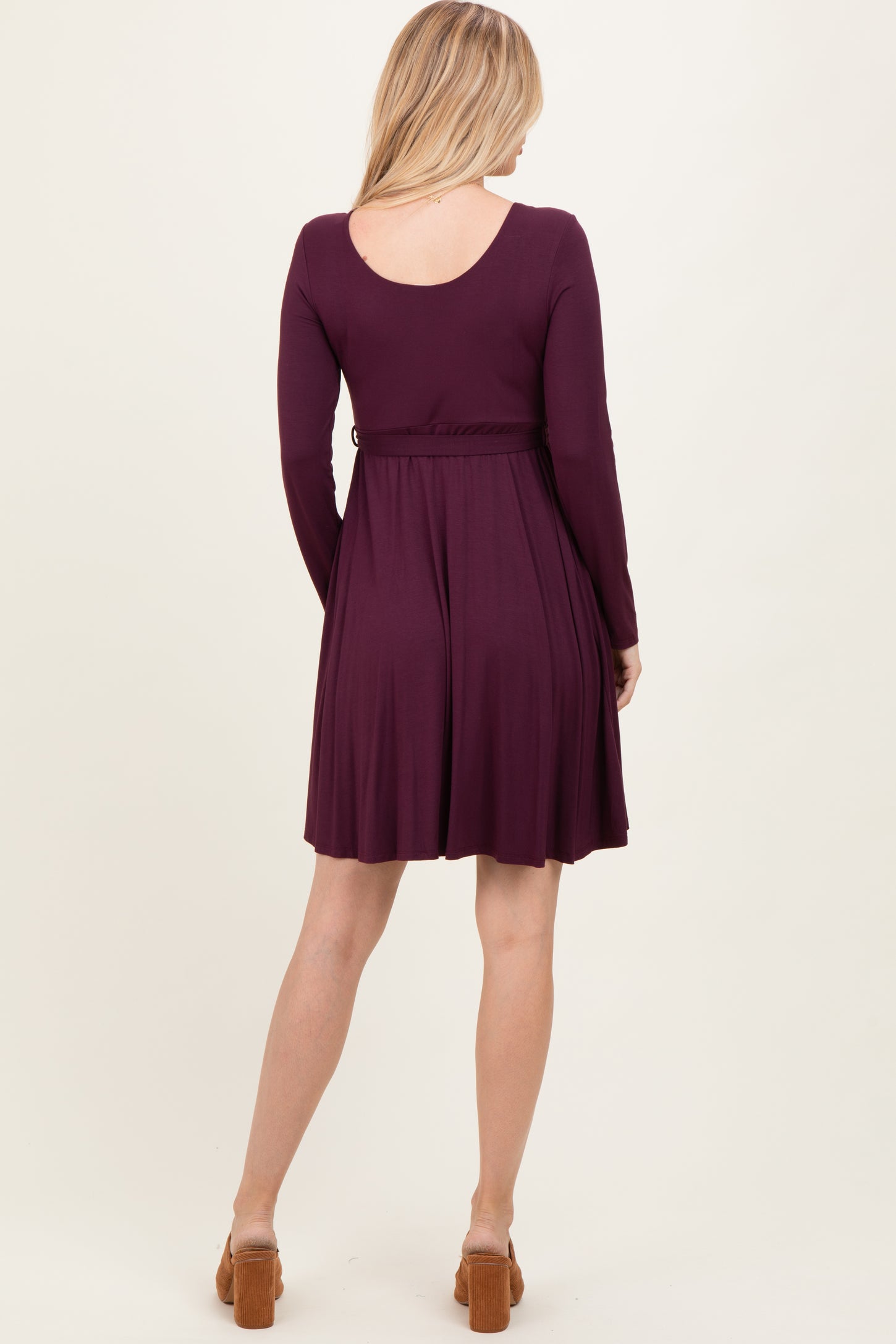 woman wearing a maroon long sleeve dress with a fitted waist and flared skirt, viewed from the back