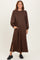 woman wearing a brown long sleeve maxi dress with puff sleeves and side pockets, standing and smiling