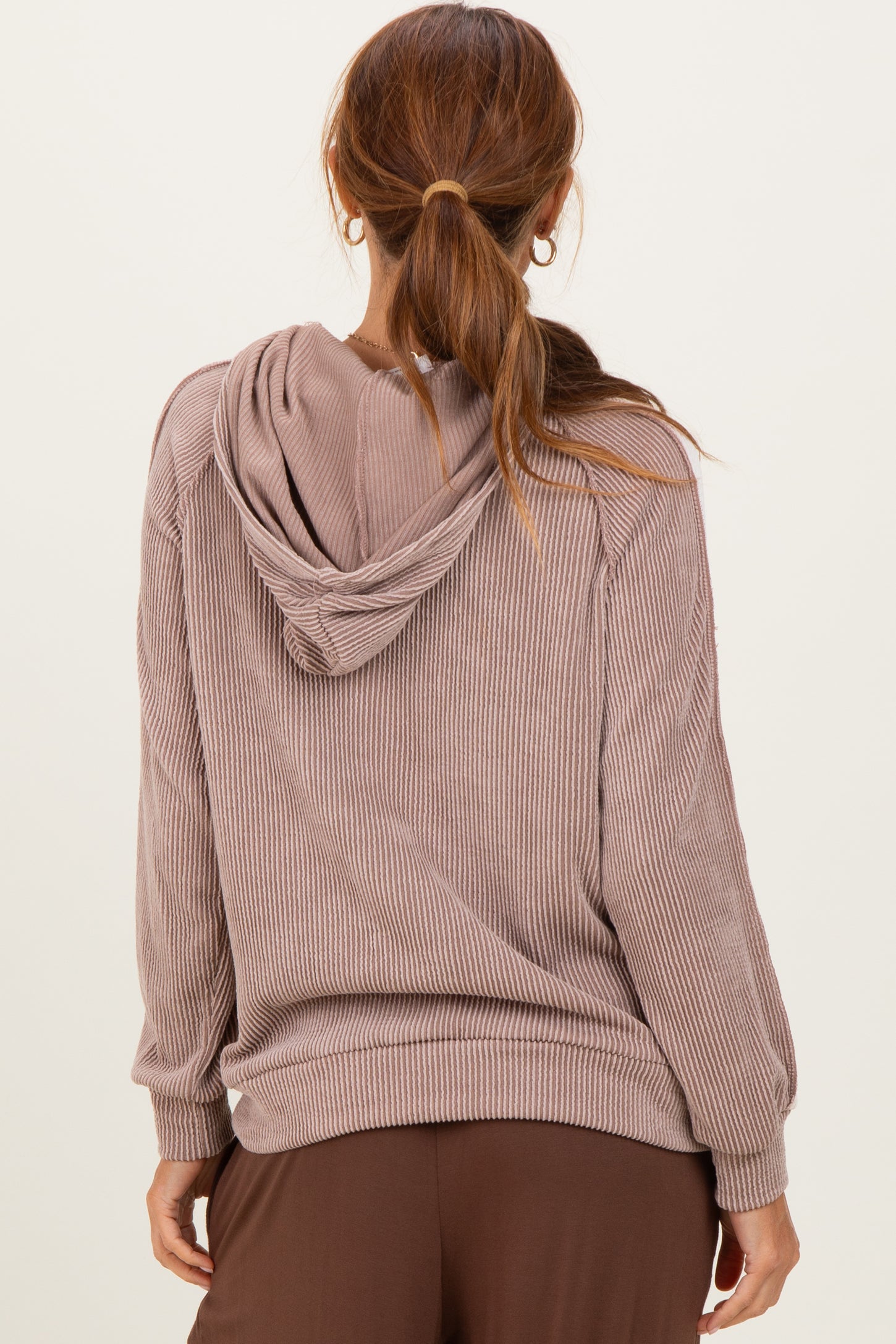 woman wearing a taupe ribbed hooded sweatshirt with a relaxed fit and long sleeves, viewed from the back