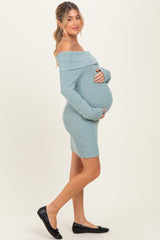 woman wearing a light blue off-the-shoulder knitted maternity dress and holding her baby bump