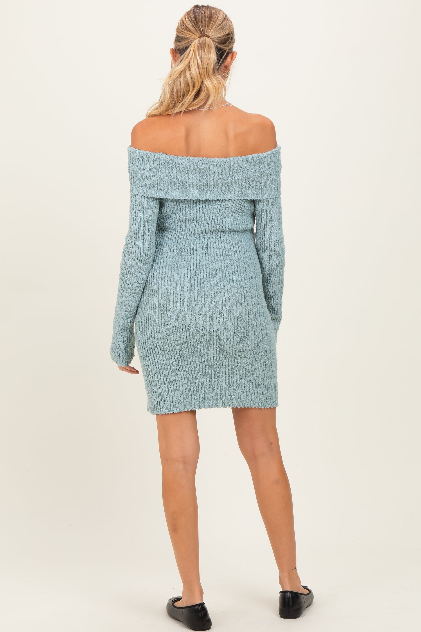 woman wearing a light blue off-the-shoulder knit maternity dress, showing a fitted silhouette from the back