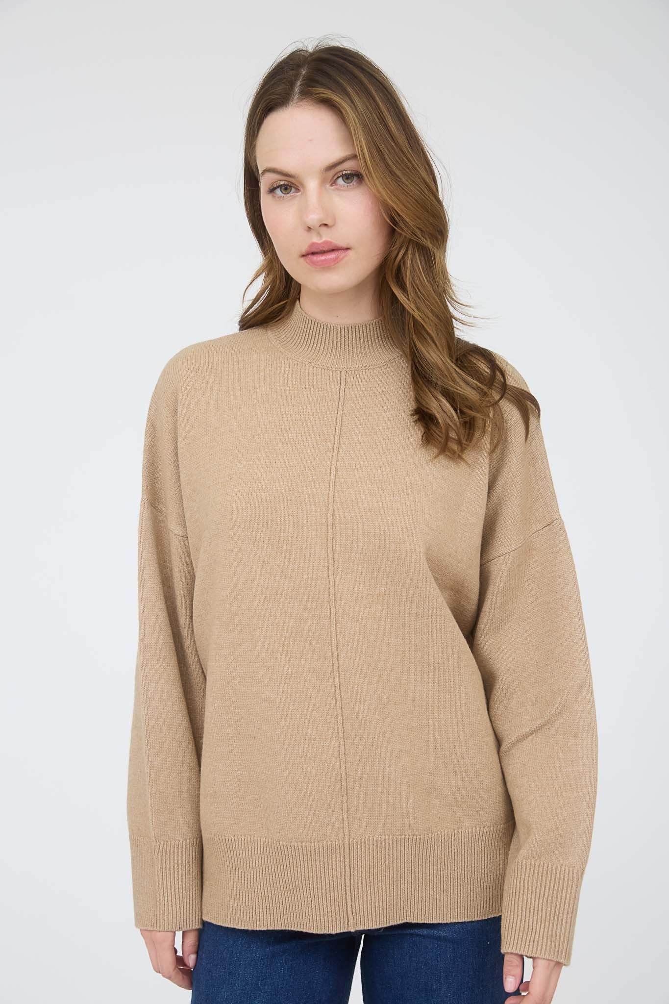 woman wearing a beige oversized sweater with a high neck and long sleeves, paired with blue jeans