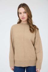 woman wearing a beige oversized sweater with a high neck and long sleeves, paired with blue jeans