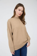 woman wearing a beige oversized knit sweater with a mock neckline and fitted cuffs paired with navy jeans