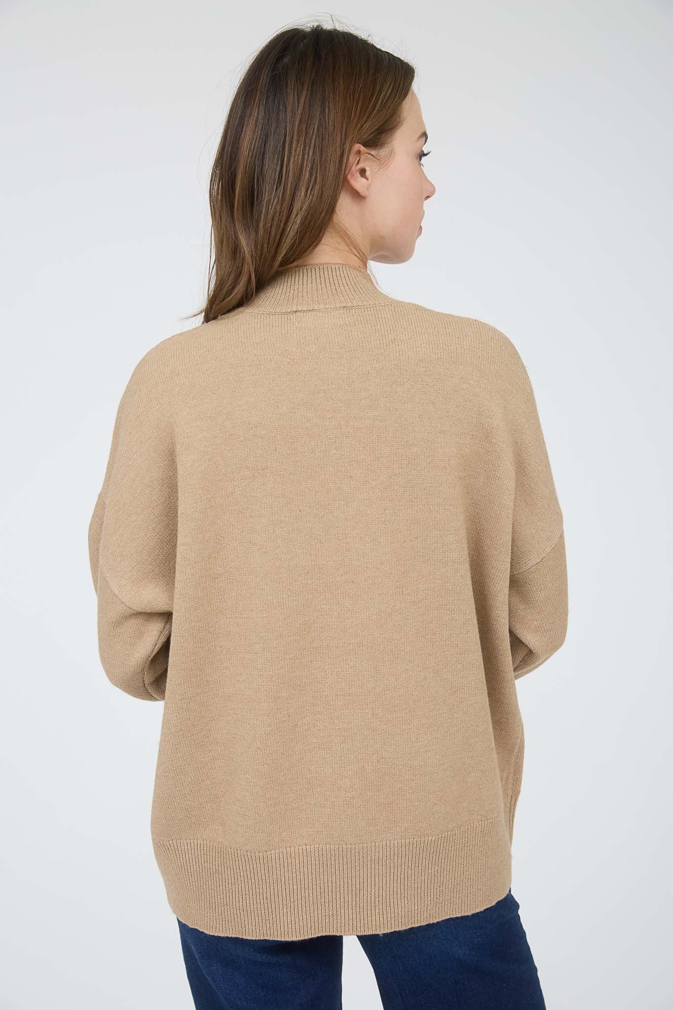 woman wearing a beige oversized sweater with a high neck and cuffed sleeves, viewed from the back
