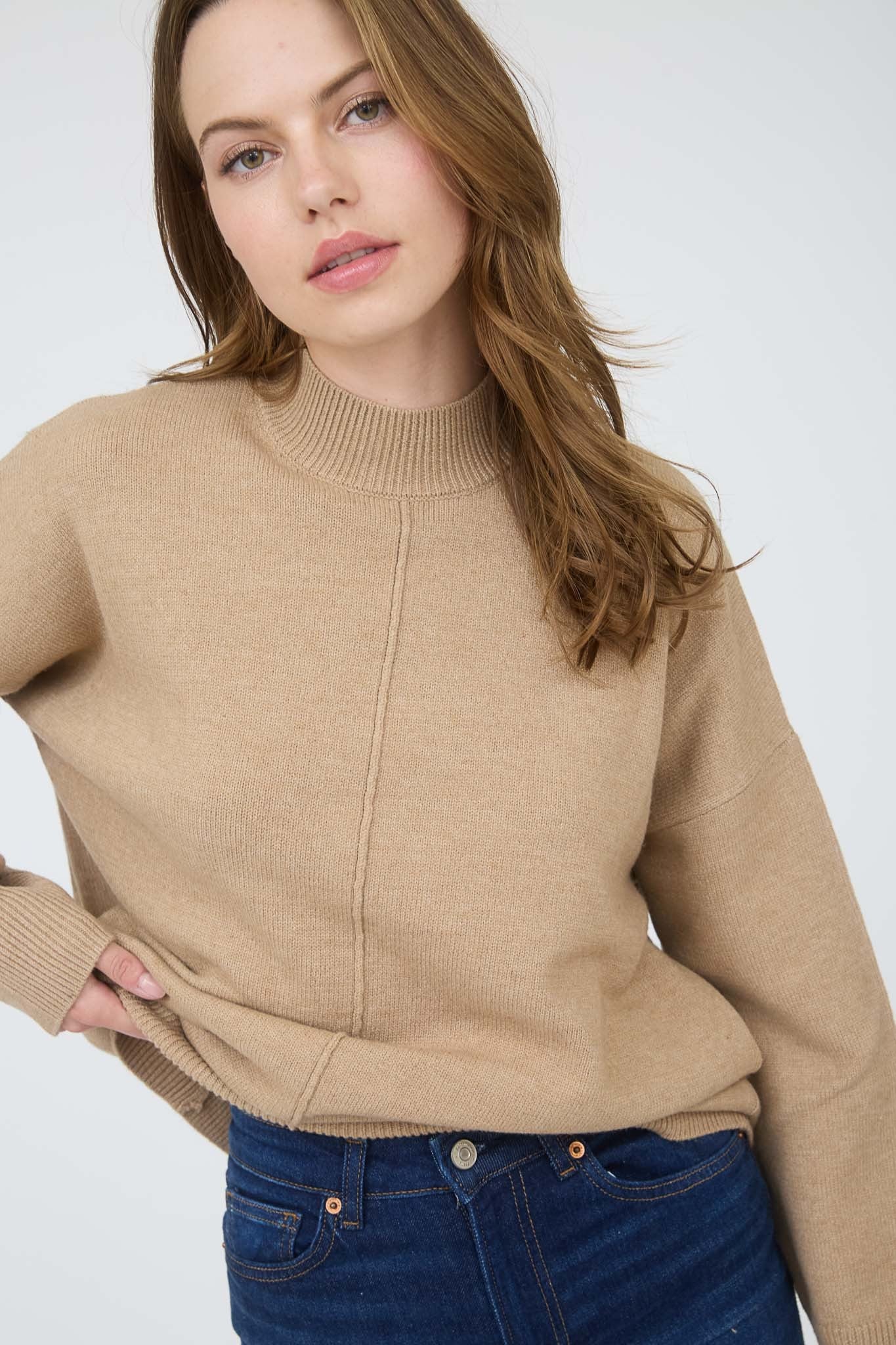 woman wearing a beige sweater with a high neck and relaxed fit, paired with dark blue jeans