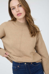 woman wearing a beige sweater with a high neck and relaxed fit, paired with dark blue jeans
