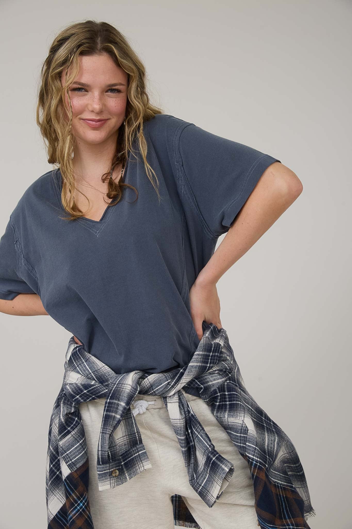 woman wearing a blue oversized v-neck t-shirt with a plaid shirt tied around her waist