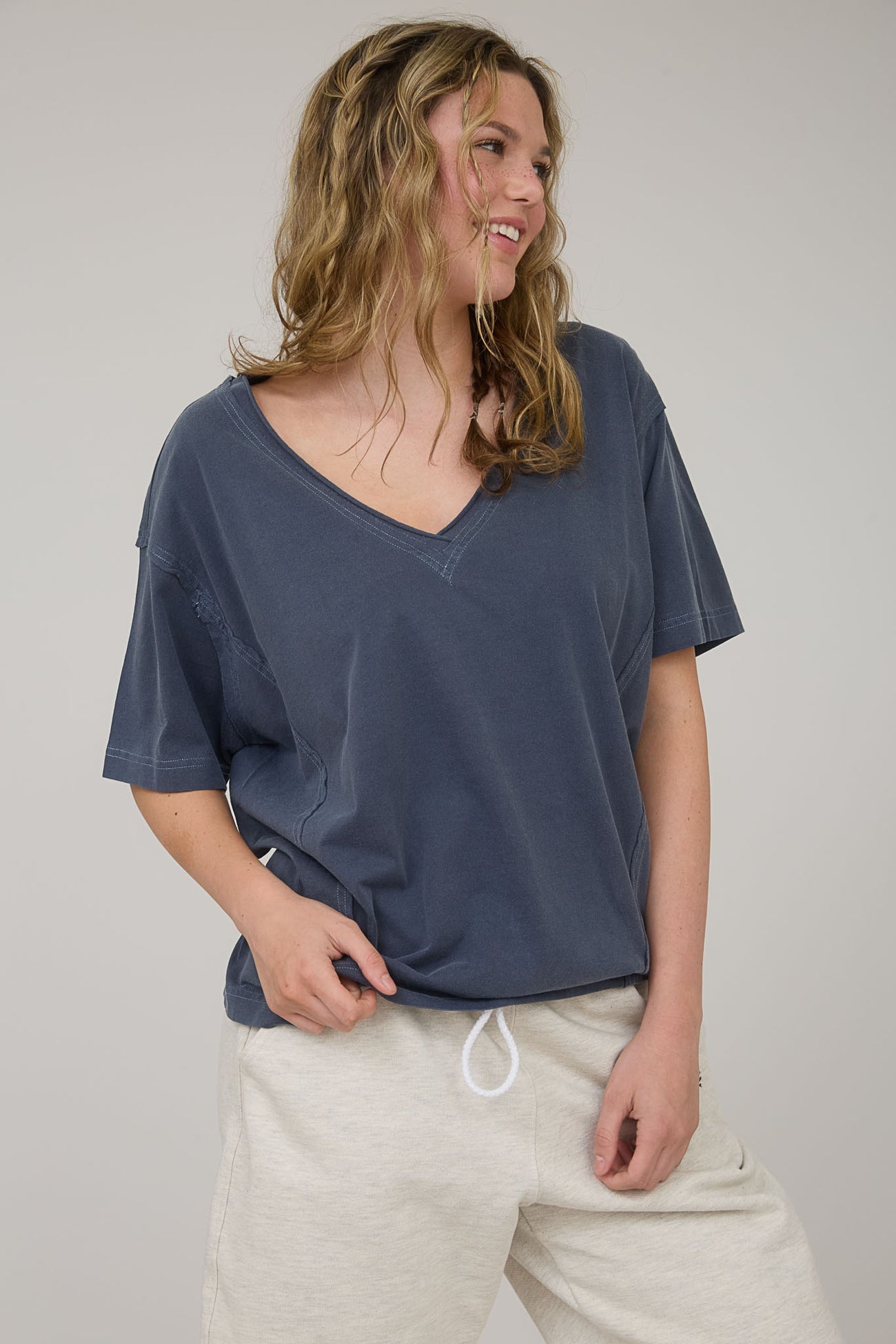 woman wearing a navy blue v-neck oversized t-shirt and light gray sweatpants, smiling and posing casually