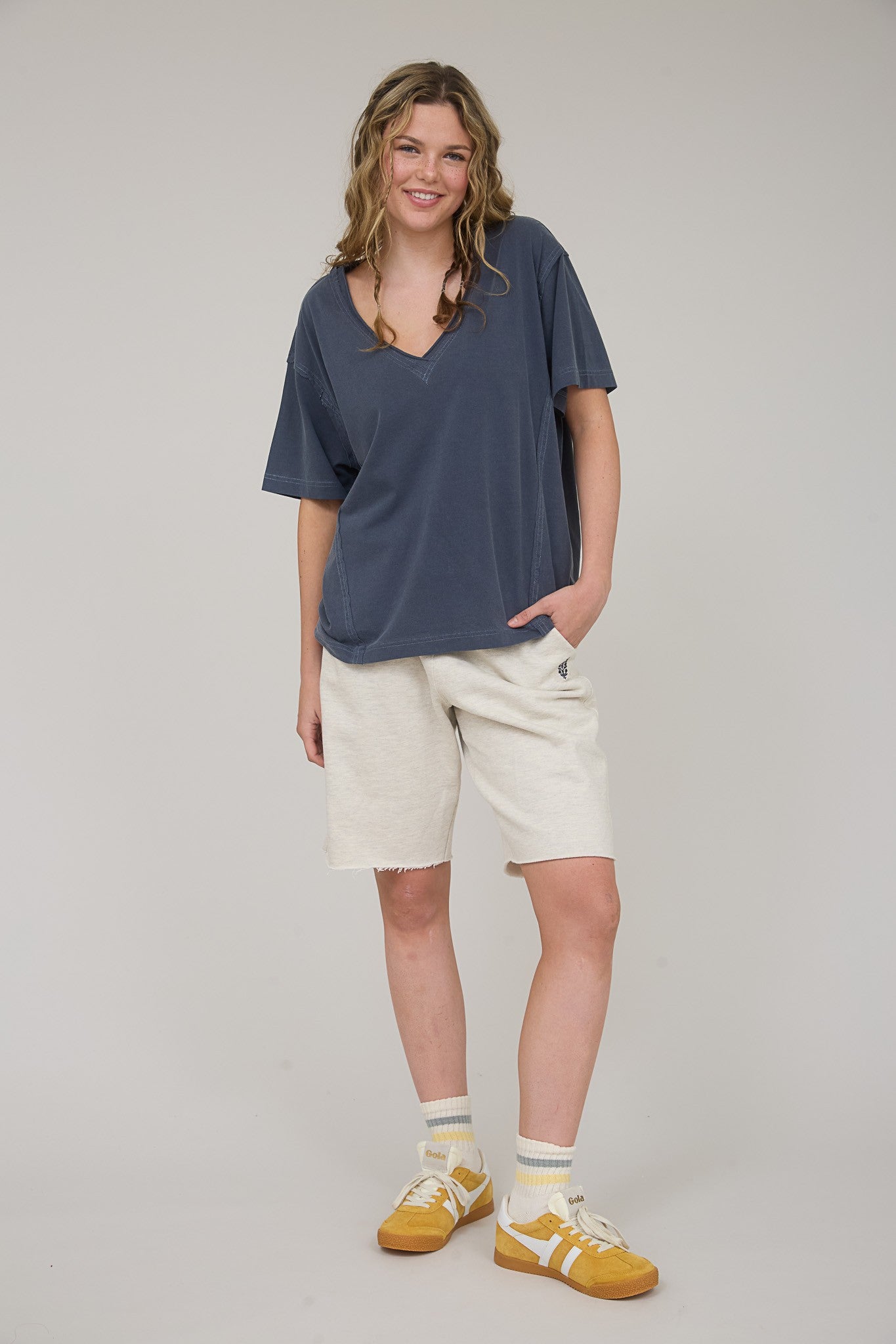 woman wearing a dark blue oversized v-neck top and cream-colored shorts, styled with yellow sneakers and socks