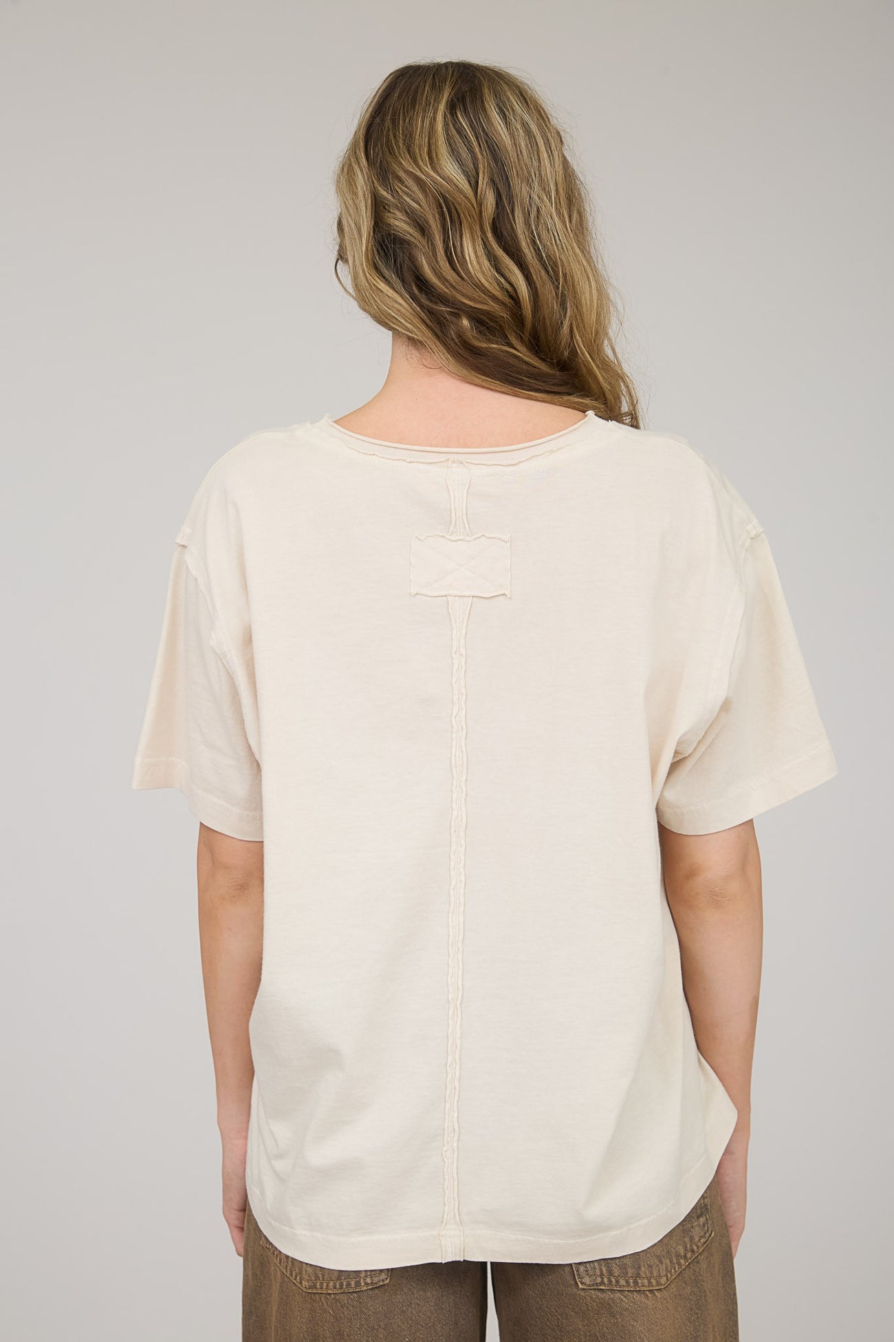 woman wearing a beige oversized t-shirt with a unique stitch detail on the back
