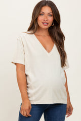 woman wearing a light beige short sleeve maternity top with a v-neck and side seam detail, showing her baby bump