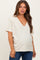 woman wearing a light beige short sleeve maternity top with a v-neck and side seam detail, showing her baby bump