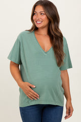 woman wearing a green v-neck maternity top and holding her baby bump