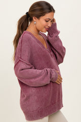 woman wearing a pink oversized maternity sweater with a v-neck and holding her baby bump