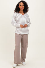 woman wearing a striped v-neck sweater in cream and gray with loose-fitting beige pants and white sneakers