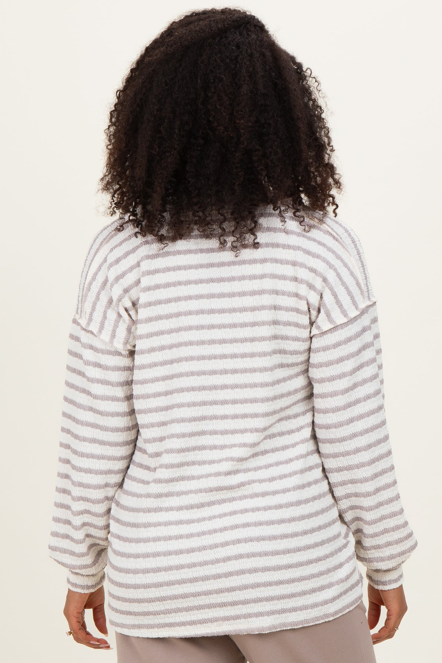 woman wearing a light grey and white striped oversized sweater with long sleeves, viewed from the back