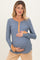 woman wearing a blue maternity top with a button-up neckline and mustard accents, holding her baby bump