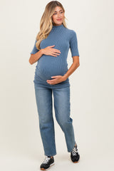 woman wearing a blue ribbed maternity top and holding her baby bump, paired with light wash straight leg jeans