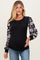 woman wearing a black maternity top with floral patterned sleeves and a visible baby bump, paired with denim jeans